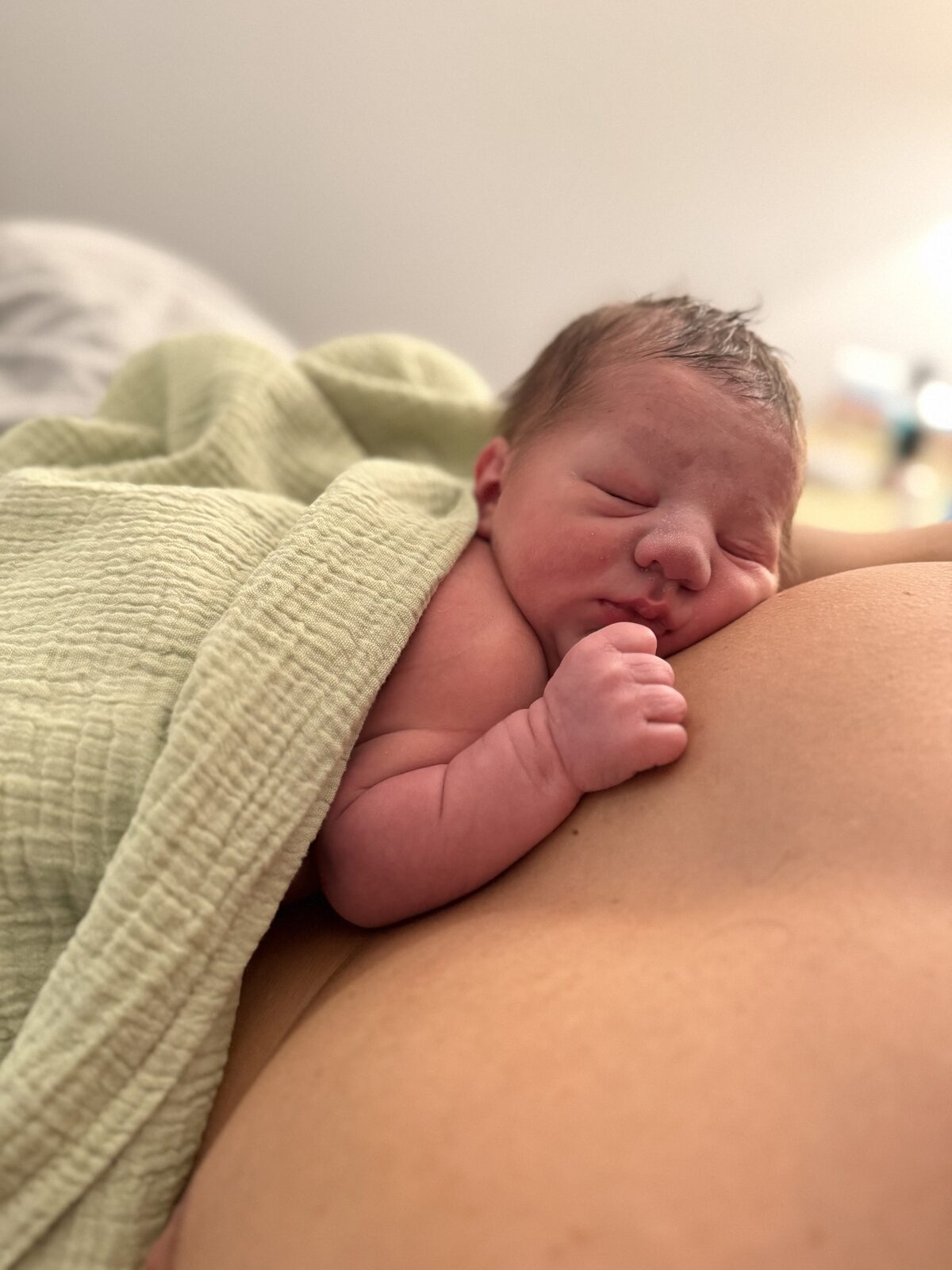 Alfie, a newborn swaddled in a green muslin, resting on his parent's chest.